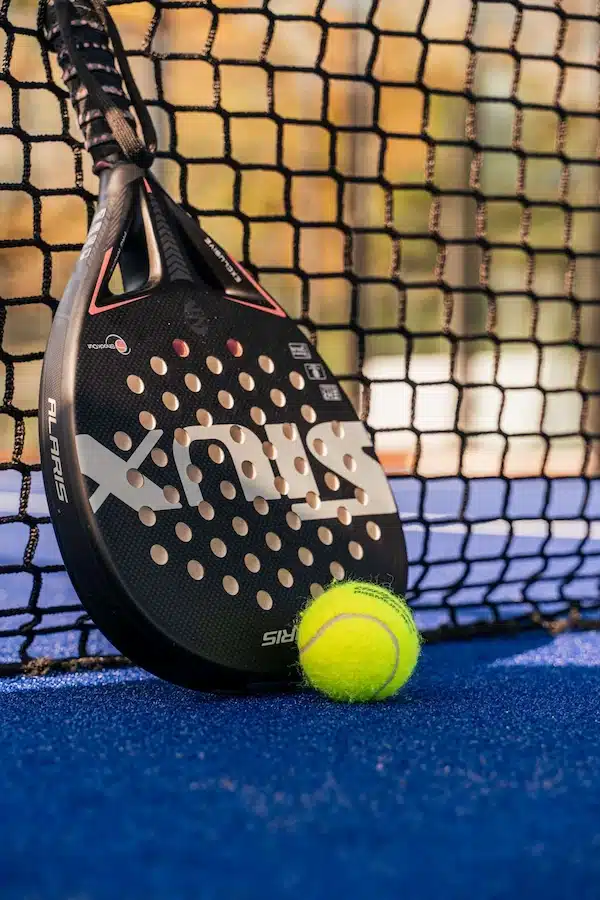 Balle devant une raquette de padel déposée par terre contre le filet